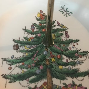 May include: A white ceramic Christmas tree serving platter with a silver stand. The tree is decorated with colorful ornaments, birds, and toys.