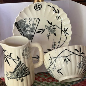 May include: A white teacup, teapot, and saucer set with black floral and fan designs. The set features a delicate floral pattern with black branches and white blossoms. The fan design is intricate and detailed, with black lines and white accents.