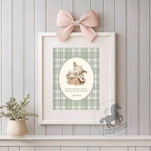 May include: A framed print featuring a watercolor illustration of a sleeping lamb. The artwork is set against a green and white plaid background, with a quote from Isaiah 40:11. A pink bow adorns the top of the frame. The print is a nursery artwork.