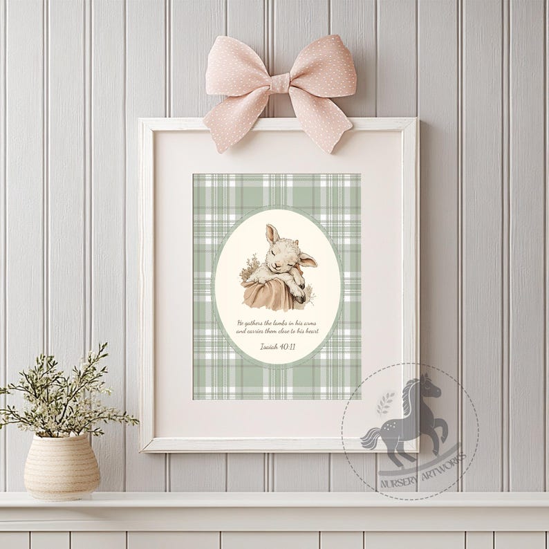 May include: A framed print featuring a watercolor illustration of a sleeping lamb. The artwork is set against a green and white plaid background, with a quote from Isaiah 40:11. A pink bow adorns the top of the frame. The print is a nursery artwork.