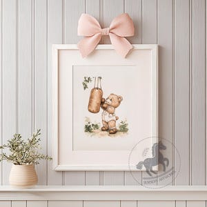 May include: A watercolor illustration of a brown bear wearing boxing gloves and punching a hanging punching bag. The bear is wearing a white onesie with a red belt. The illustration is framed in a white frame with a pink bow on top.