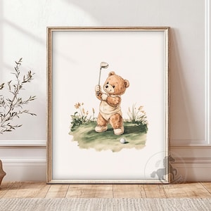 Op de afbeelding: Een aquarel-illustratie van een bruine teddybeer die een wit rompertje draagt en een golfclub vasthoudt. De beer staat op een groen grasveld met een witte golfbal voor hem.