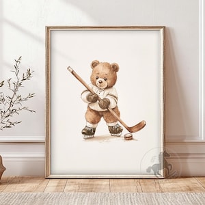 May include: A watercolor illustration of a brown teddy bear wearing a hockey jersey and holding a hockey stick. The bear is standing on a white background with a brown puck on the ground.