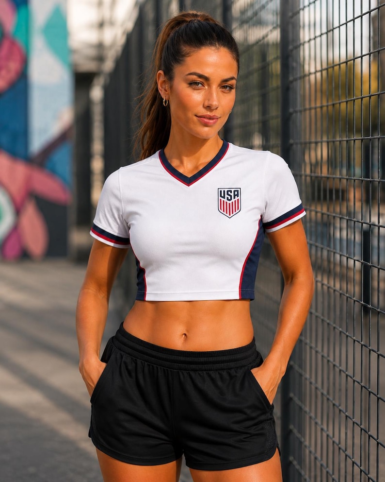 Front view of USA women's home football crop top, white with navy and red accents, fitted athletic crop top, short sleeve.