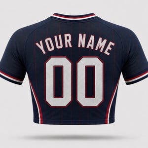 Back view of a women’s USA football away crop top in dark navy with thin red pinstripes, featuring customizable white block lettering “YOUR NAME” and number “00” with red outline, cropped fit, and athletic contouring