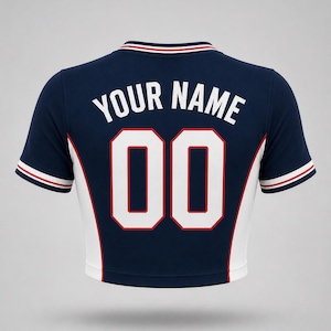 Navy blue crop top with white and red detailing. The back displays the text "YOUR NAME" above the number "00" in white with a red outline. The sleeves and collar have red and white stripes.
