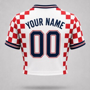 White jersey with a red and white chequered pattern on the shoulders and sleeves. The back displays the text "YOUR NAME" above the number "00" in navy blue.