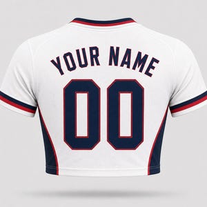 Back view of a women’s USA football home crop top in white, featuring customizable dark navy lettering “YOUR NAME” and number “00” with red outlines, navy side panels, and cropped fit