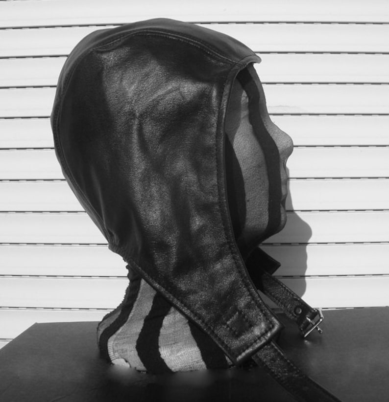 May include: A black leather hooded hat with a strap and buckle closure. The hat is worn on a mannequin head.