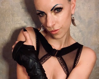 Puede incluir: Una mujer con el pelo trenzado y maquillaje con purpurina lleva un top de malla negro con un brazalete de cuero negro.