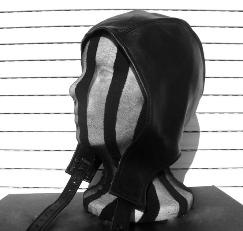May include: A black leather balaclava with a long strap. The balaclava is on a striped mannequin head.