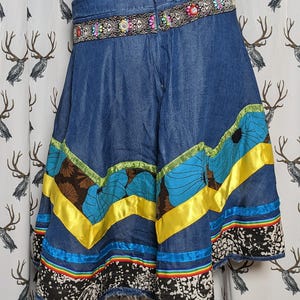 May include: A blue denim skirt with a colorful ribbon trim and a beaded belt. The skirt has a floral pattern and a layered design.