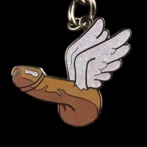 May include: A gold-colored metal keychain shaped like a cartoon figure with wings. The figure is brown and has a white outline. The wings are white with a glittery texture.