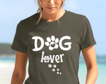 Könnte beinhalten: Dunkel olivgrünes T-Shirt mit dem weißen Text "DOG lover". Das Design beinhaltet einen Pfotenabdruck und Pfotenabdrücke. Das Shirt ist ein kurzärmeliges Rundhals-Shirt.