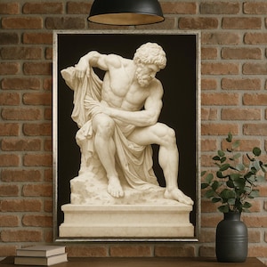 May include: A framed print of a classical sculpture showing a seated, muscular male figure draped in cloth. The sculpture is white, with a dark background. The frame is silver. The print is on a wooden table against a brick wall.