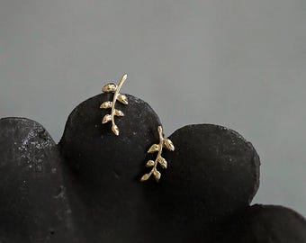 Könnte beinhalten: Ein Paar goldene Blattohrringe, jedes mit einem zarten Zweigdesign mit kleinen Blättern.