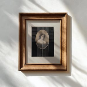 Puede incluir: Un retrato vintage enmarcado. La imagen presenta un retrato ovalado en tonos sepia de una persona sobre un fondo a rayas blancas y negras. El marco es de madera con un acabado cálido y natural, y está montado en una pared blanca.