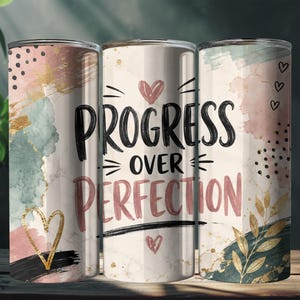 May include: A cylindrical tumbler featuring a white marble background with abstract watercolor splashes in pink, teal, and gold. The text "PROGRESS OVER PERFECTION" is printed in black and pink, accented by small hand-drawn hearts and gold leaf motifs.