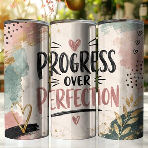 May include: Three cylindrical tumblers featuring a white marble background with abstract watercolor splashes in pink, sage green, and gold. The center tumbler displays the black text "PROGRESS OVER PERFECTION" with small pink hearts and black dots.