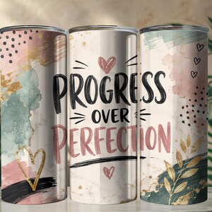 May include: Three cylindrical tumblers featuring a watercolor design in shades of pink, teal, and gold. The center tumbler displays the black text "PROGRESS OVER PERFECTION" with small heart icons, while the others show abstract brushstrokes, gold leaf accents, and black polka dots.