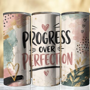 May include: Three cylindrical tumblers featuring a cream-colored marble background with abstract watercolor splashes in dusty pink, sage green, and black. The text "PROGRESS OVER PERFECTION" is printed in black and pink, accented by gold hearts and leaves.