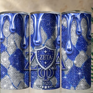 Può includere: Un bicchiere cilindrico con un motivo a rombi glitterati blu e argento e un effetto gocciolante blu sulla parte superiore. Al centro è presente uno stemma blu con la scritta ZETA PHI BETA e l'anno 1920, circondato da perle bianche.