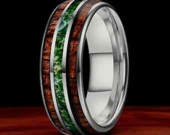 Könnte beinhalten: Ein silberner Ring mit einem einzigartigen Design. Der Ring hat ein zentrales Band aus grünem Stein, flankiert von Bändern aus dunkelbraunem Holz. Der Ring hat eine polierte, metallische Oberfläche, und die Holzmaserung ist sichtbar.