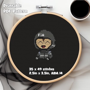 May include: A cross-stitch pattern of a cartoon character in a wooden embroidery hoop. The character wears a helmet with the letters "FIA" and glasses. The pattern is 2.5 inches by 3.5 inches and has 35 x 49 stitches. The text "Printable PDF Pattern" is at the top.