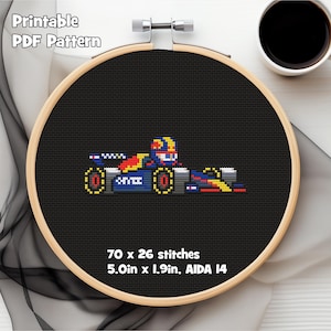 Può includere: Schema a punto croce di un'auto da corsa di Formula 1 in un telaio da ricamo in legno. L'auto è blu, rossa e gialla. Il testo "Printable PDF Pattern" è in alto. Lo schema misura 12,7 cm x 4,8 cm e ha 70 x 26 punti.