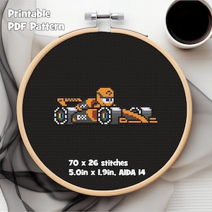 Może przedstawiać: Wzór haftu krzyżykowego bolidu Formuły 1 w kolorze pomarańczowym, szarym i białym, na czarnym tle w drewnianym tamborku. U góry znajduje się napis "Printable PDF Pattern". Wzór ma wymiary 12,7 cm x 4,8 cm.