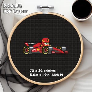 May include: Cross-stitch design of a red Formula 1 race car with a driver in a helmet, set against a black background. The design is in a wooden embroidery hoop. Text at the top reads "Printable PDF Pattern". The pattern is 12.7cm x 4.8cm.