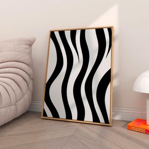 Può includere: Una stampa artistica incorniciata con un motivo ondulato in bianco e nero, che ricorda le strisce di una zebra. L'opera d'arte è presentata in una cornice di legno marrone chiaro. La stampa aggiunge un tocco moderno a qualsiasi spazio interno.