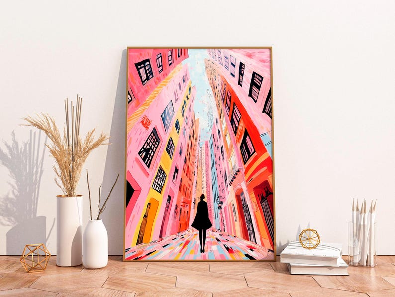 May include: A painting of a colorful city street with tall buildings and a person walking down the middle. The buildings are painted in shades of pink, orange, and yellow, and the street is a mix of pink, blue, and yellow.