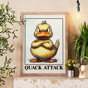 Può includere: Opera d'arte incorniciata con un'anatra gialla illustrata con un'espressione arrabbiata e le braccia incrociate. L'opera presenta le parole "QUACK ATTACK" in grassetto nero in basso. La cornice è di colore marrone chiaro.