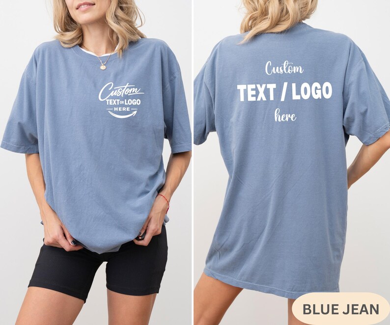 May include: A blue jean coloured t-shirt with the text "Custom TEXT / LOGO here" printed on the front and back. The front of the shirt has a curved text design. The shirt is a short-sleeved, oversized fit.