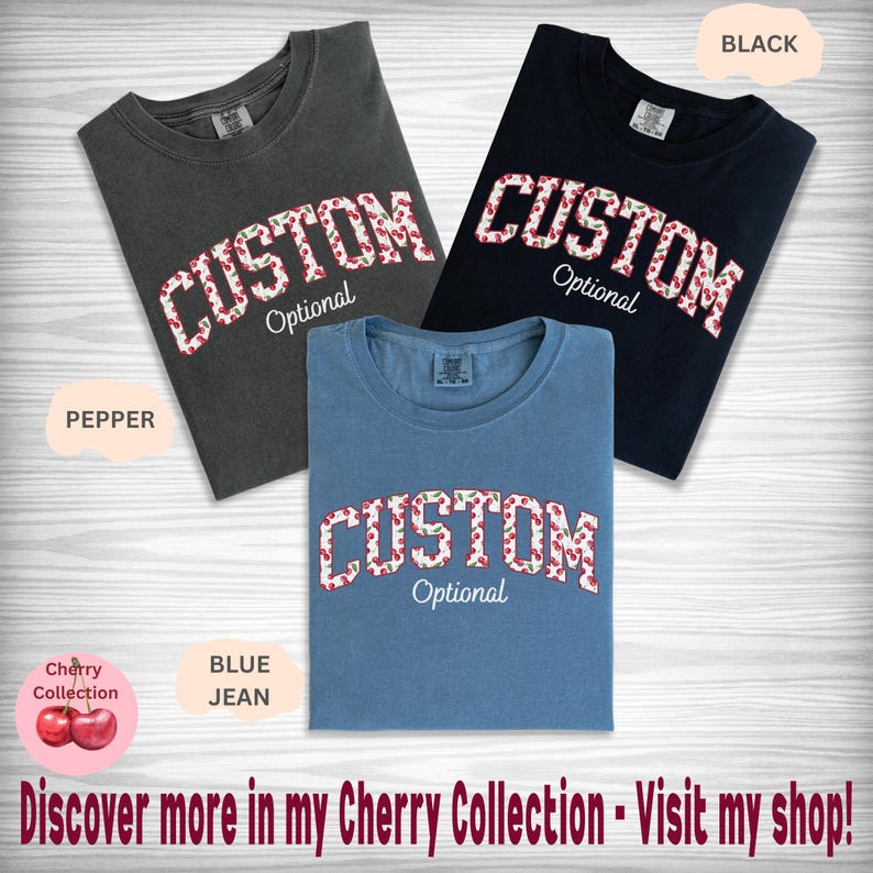 Pu&ograve; includere: Tre magliette a girocollo nei colori pepper, nero e blue jean. Ogni maglietta presenta la parola CUSTOM in un carattere con motivo a ciliegie, con la parola Optional scritta sotto in corsivo bianco. Le magliette sono disposte su una superficie in legno chiaro.
