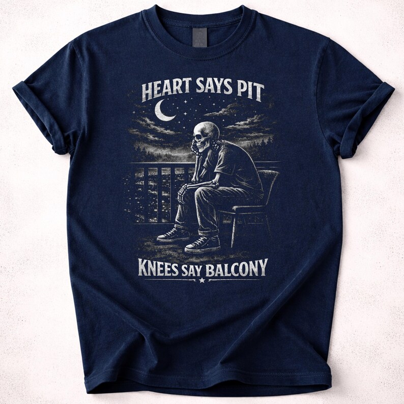 Pu&ograve; includere: T-shirt blu navy con grafica di uno scheletro seduto su un balcone, con il testo "HEART SAYS PIT" e "KNEES SAY BALCONY". Il design include una luna e un paesaggio urbano.