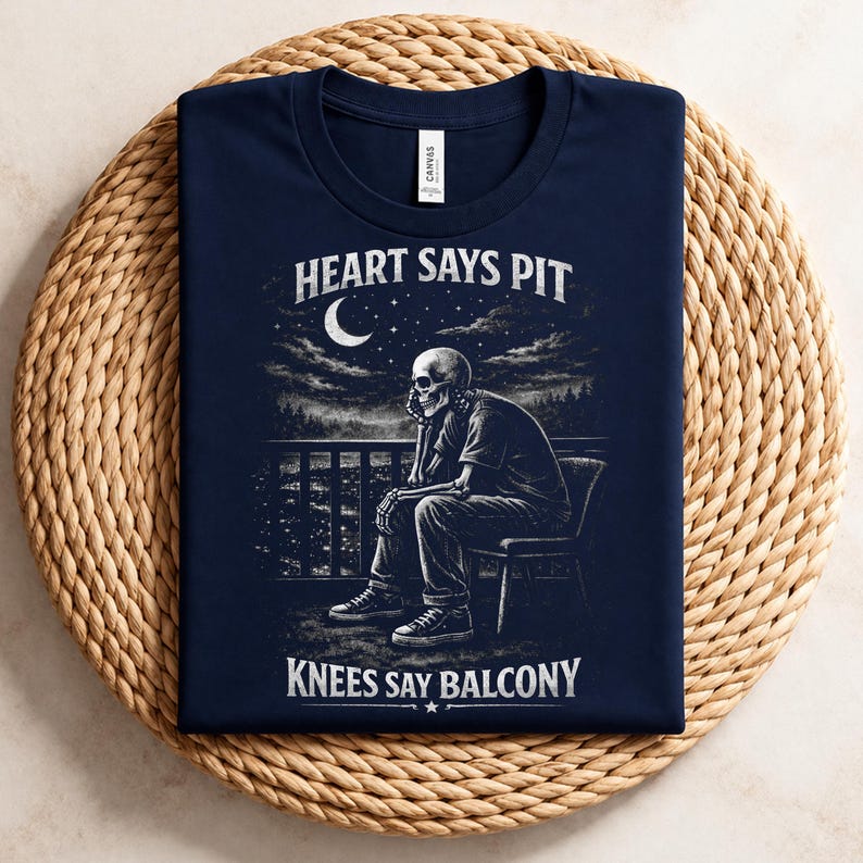 Pu&ograve; includere: T-shirt blu navy con grafica in bianco e nero di uno scheletro seduto su un balcone, con la scritta "HEART SAYS PIT" e "KNEES SAY BALCONY". Il design &egrave; ambientato su uno sfondo di cielo notturno.