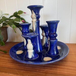 May include: A ceramic candle holder with a deep blue glaze and white accents. The holder features five candle cups of varying heights, set on a matching blue plate. The design is a mix of modern and rustic styles.