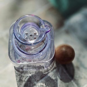 May include: A clear plastic bottle with a lid that has a strainer. The bottle has a label that says "Java" on it.