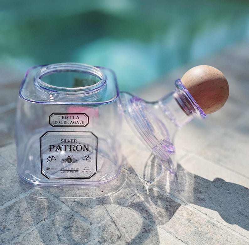 May include: A clear plastic bottle with a wooden stopper. The bottle is labeled "Tequila 100% de Agave" and "Silver Patron".