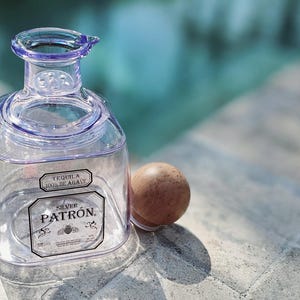 May include: A clear glass bottle with a silver cap and a label that reads "Tequila 100% de Agave" and "Silver Patron".