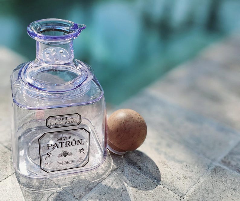May include: A clear glass bottle with a silver cap and a label that reads "Tequila 100% de Agave" and "Silver Patron".