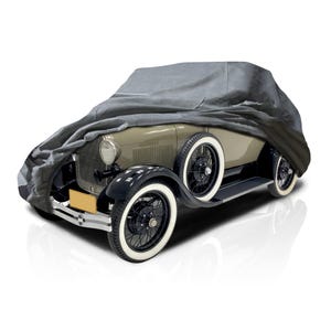 Pode incluir: Um carro clássico vintage, parcialmente coberto por uma capa cinza. O carro tem uma carroceria verde clara, para-lamas pretos e pneus com faixas brancas. As rodas têm raios pretos. Uma placa amarela é visível.