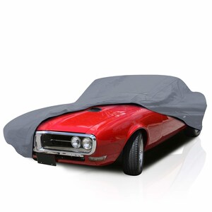 Può includere: Un'auto classica rossa è parzialmente coperta da un telo grigio. Il telo copre il cofano e il tetto, proteggendo il veicolo. L'auto ha finiture cromate e una targa nera.