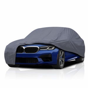 May include: A grey car cover over a blue car. The cover is made of a smooth, reflective material. The front of the car, including the headlights and grill, is visible. The car is parked on a white surface.