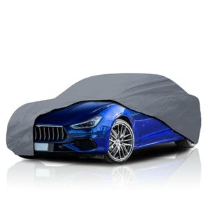 Op de afbeelding: Een grijze autohoes gedeeltelijk over een blauwe sportwagen gedrapeerd. De voorkant van de auto, inclusief de koplampen en wielen, is zichtbaar. De hoes lijkt gemaakt te zijn van een lichtgewicht, waterbestendig materiaal, ontworpen om het voertuig te beschermen tegen de elementen.