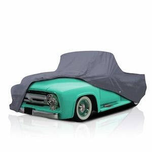 Peut inclure: Un pick-up vintage turquoise est partiellement recouvert d'une housse de voiture grise. Le camion a des pare-chocs chromés et des pneus à flancs blancs. La housse de voiture recouvre le capot et la cabine du véhicule.