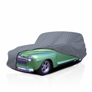 May include: A gray car cover partially draped over a vintage green car. The car has chrome accents, a classic grill, and chrome wheels. The cover protects the car from the elements.
