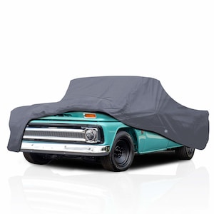 Peut inclure: Une housse de voiture grise recouvrant une camionnette vintage turquoise. La housse masque la majeure partie du véhicule, mais la calandre avant, le pare-chocs et les pneus sont visibles. Le camion a des pneus noirs et des garnitures chromées.
